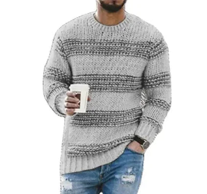 A man wearing a stylish gray and black striped knitted sweater with a cozy, textured design. He holds a white coffee cup in one hand while the other is casually placed in the pocket of his distressed blue jeans. The outfit has a relaxed and modern casual vibe, ideal for cool weather.