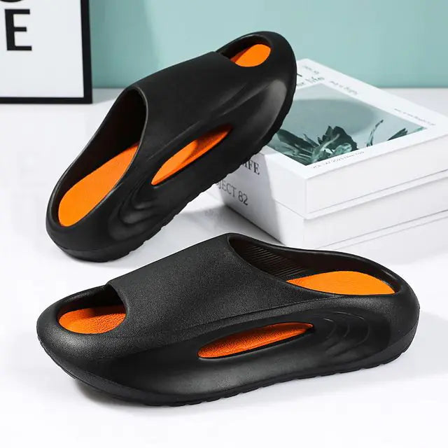A pair of stylish black slip-on sandals with purple cushioned insoles, featuring cutout designs on the sides and toes, displayed on a white surface next to stacked books.