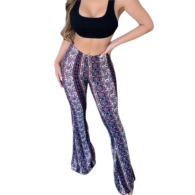 Woman wearing a black crop top and high-waisted, flared bohemian print pants with a mix of geometric and floral patterns in shades of purple, white, and maroon, posing with one hand on her hip