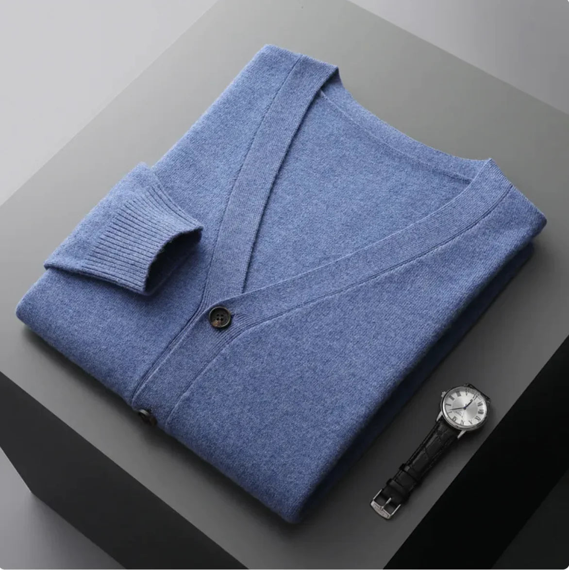 A neatly fold shirt on a black  surface with a black leather wrist-watch beside it