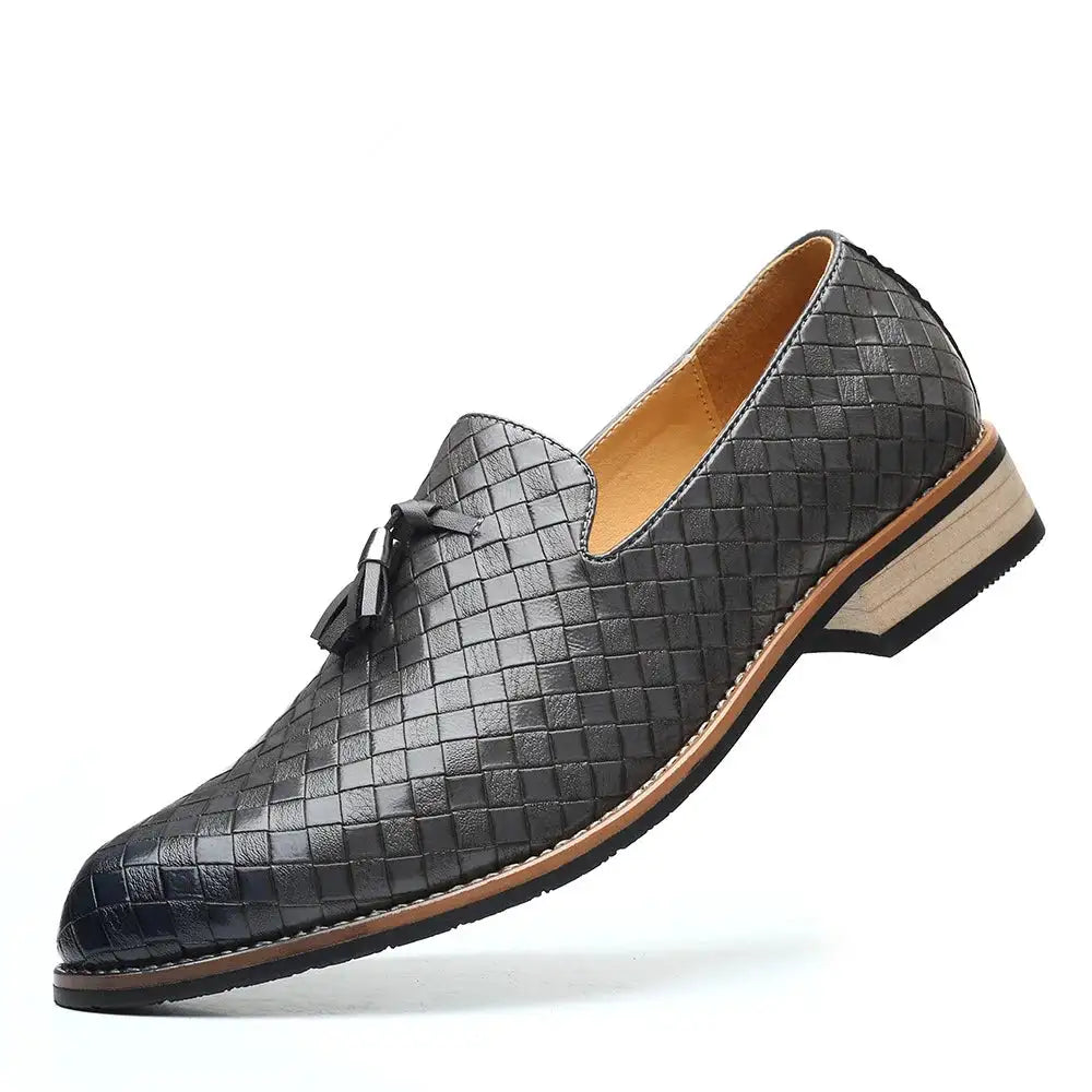 A stylish navy blue woven leather loafer with tassel accents, featuring a light tan interior and a stacked sole with a black rubber outsole, displayed against a white background.