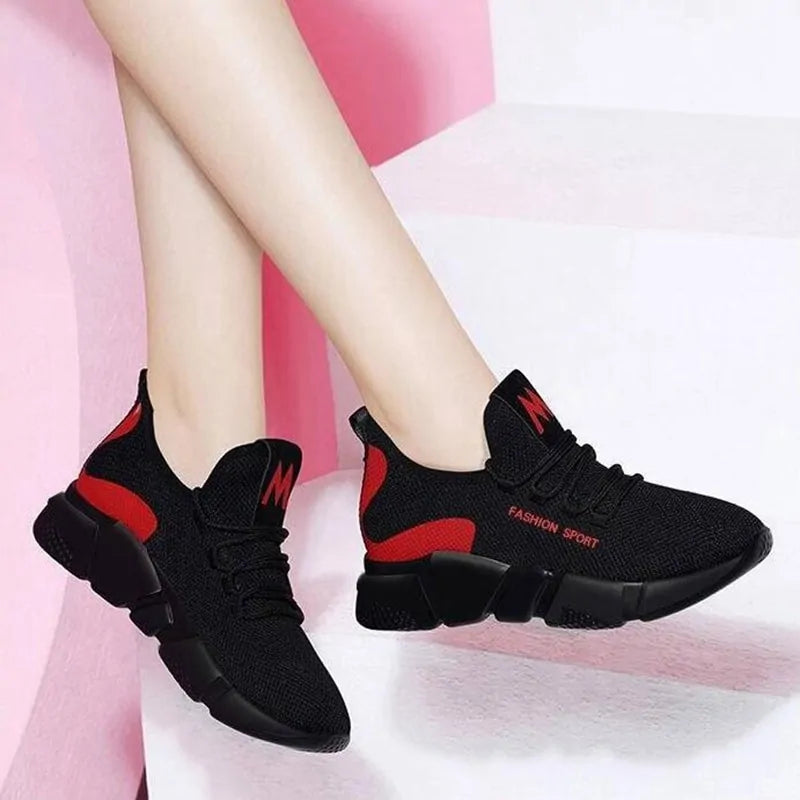 A pair of stylish black mesh sneakers worn with jeans. The shoes feature colorful embroidered details including a red and yellow daisy on the side and multicolored accents (red, blue, yellow) on the sole. The tongue displays a purple and red logo with the word "FASHION." The sneakers have a sleek, breathable design and a casual, trendy aesthetic.