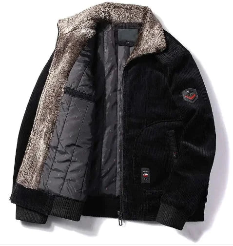 A stylish corduroy jacket with a plush fur-lined collar and inner lining is displayed against a white background. The jacket features a quilted black interior for added warmth, ribbed black cuffs and hem, and a zippered front closure. It has two side pockets, one of which has a small black and red tag. A subtle embroidered patch is visible on the left sleeve, adding a touch of detail to the design