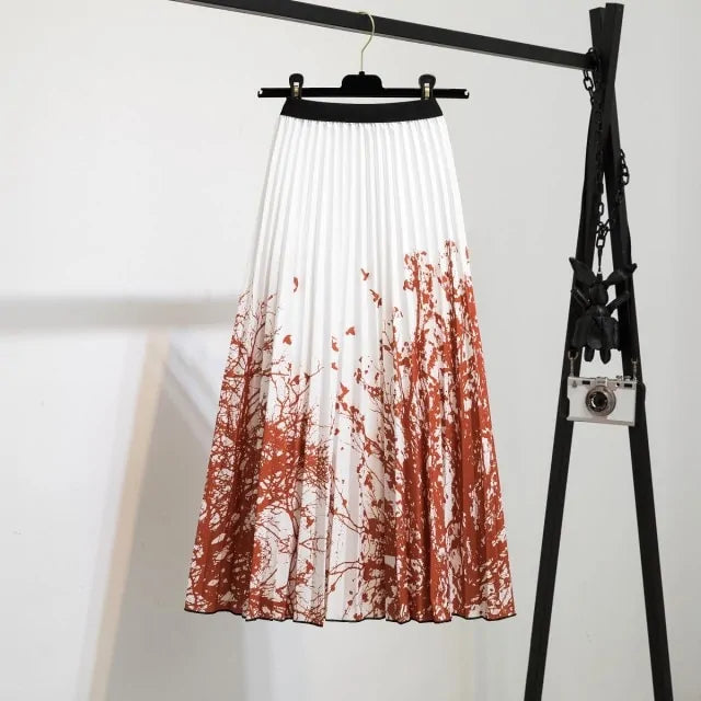 Pleated midi skirt with a gradient design, transitioning from dark black at the waistband to a soft blush pink at the hem, hanging on a black clothing rack next to a vintage-style camera.