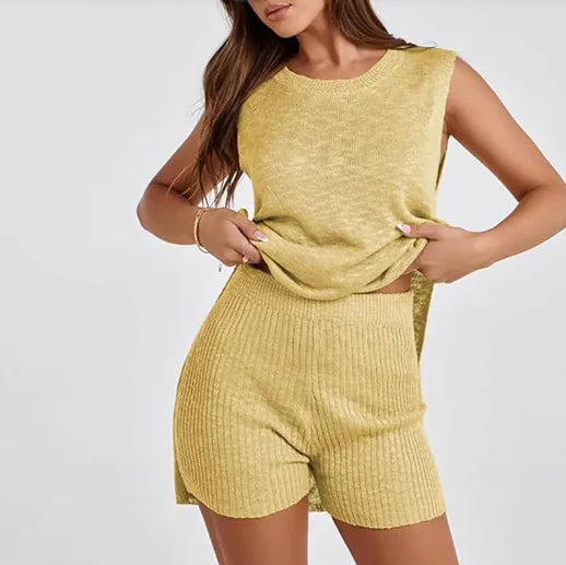 Woman standing on a sandy beach wearing a sleeveless, rust-orange mini dress with a relaxed fit and subtle ribbed texture on the sides, with the ocean and rocks in the background under a clear blue sky.