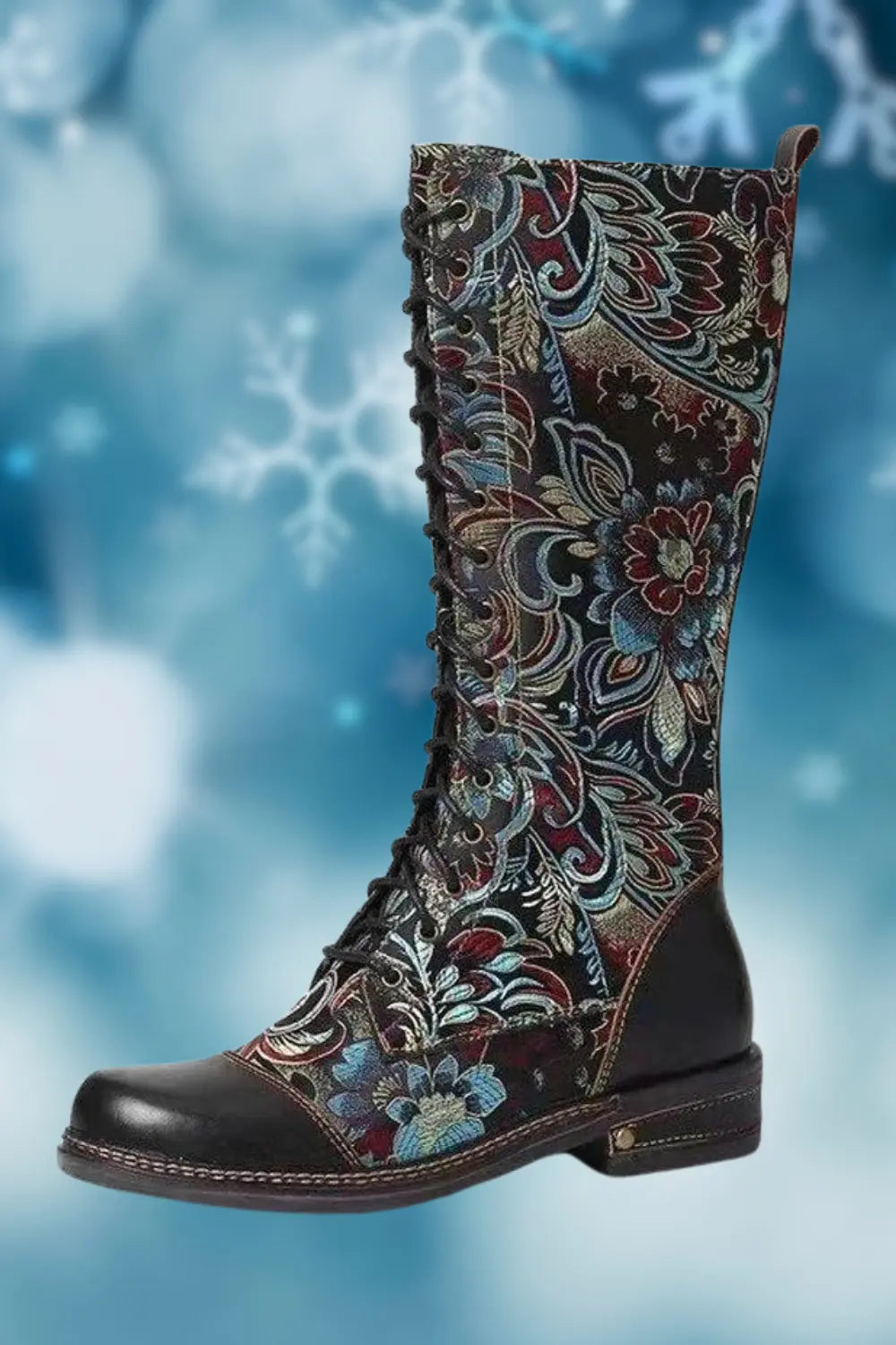 A stylish knee-high lace-up boot with a vibrant blue and red floral pattern, featuring leather accents on the toe and heel, set against a soft blue background with snowflake motifs.