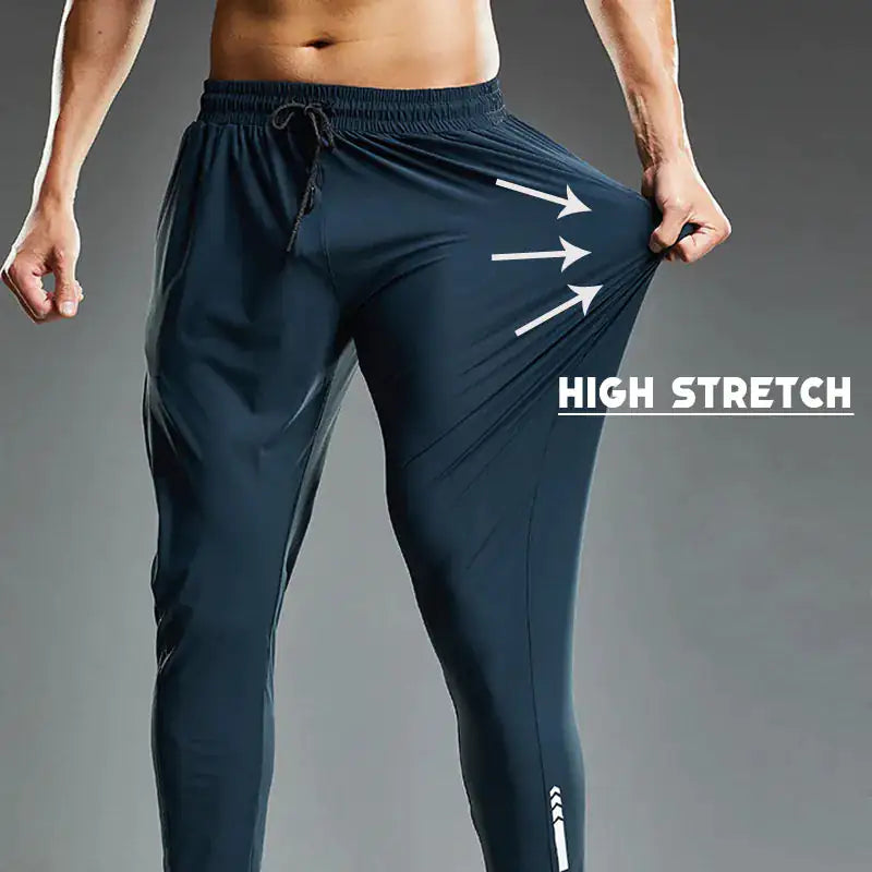 A muscular man wearing dark athletic joggers demonstrates the high-stretch capability of the fabric by pulling the side of the pants outward. The image has a dark gradient background, and bold white text that reads "HIGH STRETCH" with three arrows pointing to the stretched fabric, emphasizing its elasticity. The joggers feature an elastic waistband with a drawstring and a sleek, tapered fit, ideal for sports and activewear.