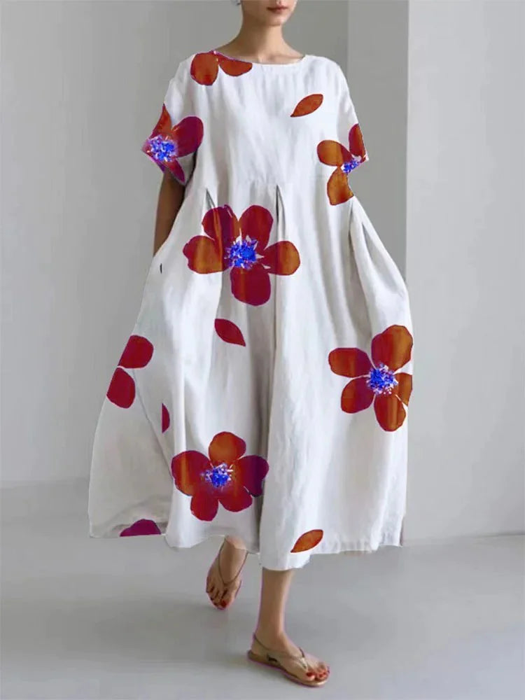 Woman wearing a loose-fitting, white midi dress with short sleeves, featuring bold red-orange floral prints accented with blue centers, paired with flat sandals.