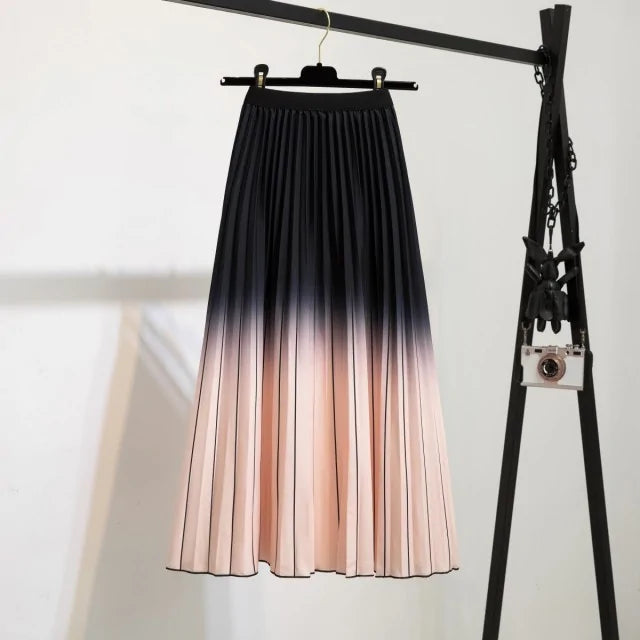 Pleated midi skirt with a gradient design, transitioning from dark black at the waistband to a soft blush pink at the hem, hanging on a black clothing rack next to a vintage-style camera.