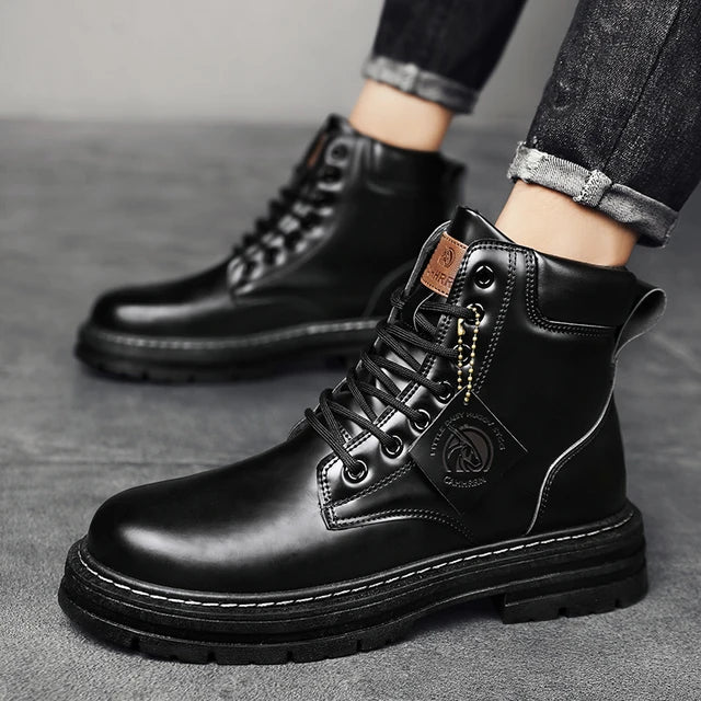 A pair of sleek black leather ankle boots with rugged rubber soles, lace-up fronts, and metal eyelets, displayed on a gray fabric surface with one boot propped up on a vintage-style book for presentation.