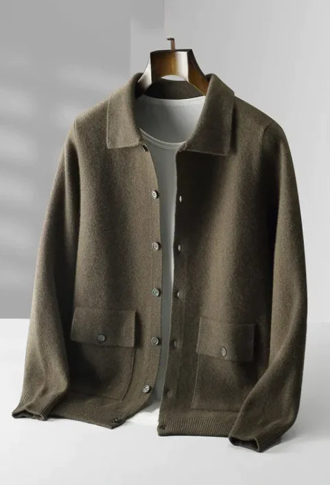 A dark olive green button-up knit cardigan with a classic collar, two front pockets with buttoned flaps, and ribbed cuffs and hem. The cardigan is layered over a white T-shirt and displayed on a wooden hanger, presenting a sophisticated and understated style.
