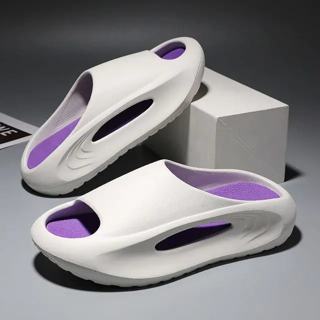 A pair of stylish black slip-on sandals with purple cushioned insoles, featuring cutout designs on the sides and toes, displayed on a white surface next to stacked books.
