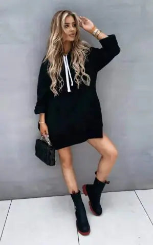 Stylish woman wearing an oversized bright orange hoodie with white drawstrings, paired with white shorts, green and white sneakers, a black Balenciaga baseball cap, and a black quilted handbag, posing against a light grey background.