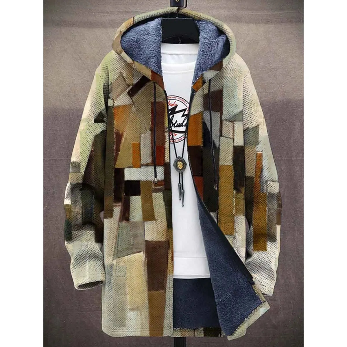 A stylish hooded jacket featuring an abstract geometric patchwork design in earthy tones of brown, beige, and olive green. The jacket has a warm fleece-lined interior, a front zipper, and adjustable drawstrings on the hood. It is layered over a white T-shirt with a circular graphic print and accessorized with a long pendant necklace.