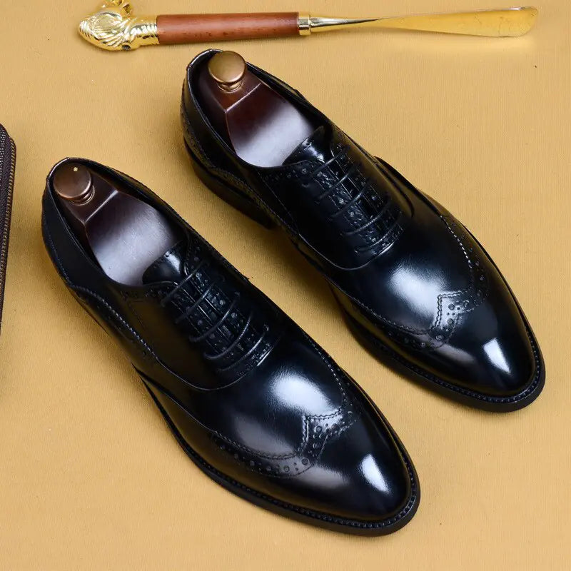 A pair of elegant burgundy leather loafers with a glossy finish. The shoes feature gold-toned metal horsebit detailing across the uppers and are displayed with wooden shoe trees inserted. They have a sleek, elongated silhouette with subtle stitching along the toe cap. The loafers are placed on a dark surface, partially framed by a wooden picture frame, emphasizing their classic and sophisticated style.