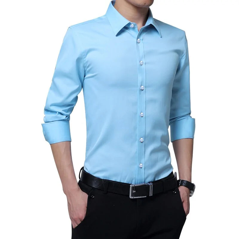 A man wearing a fitted light blue dress shirt with long sleeves rolled up to his elbows. The shirt has a button-up front and a structured collar, giving it a polished appearance. He pairs it with black dress pants, a black leather belt with a silver buckle, and a wristwatch on his left wrist. His hands are casually tucked into his pockets, and his face is cropped out of the frame, focusing on the outfit.
