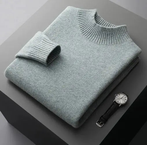 A neatly folded beige knitted sweater with a ribbed high collar and cuffs, placed on a dark grey surface. Beside the sweater, a classic wristwatch with a black leather strap and a silver dial is positioned, adding a touch of elegance to the composition.