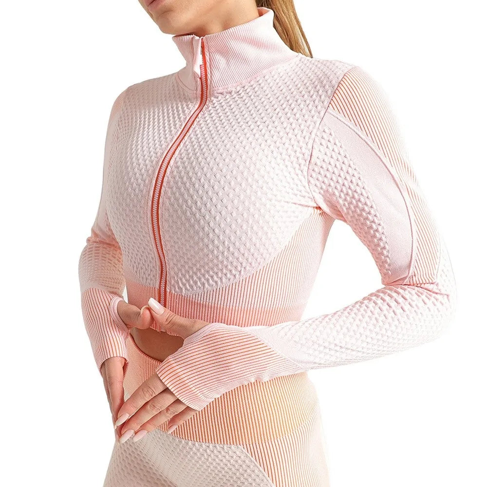 Woman wearing a seamless, textured long-sleeve athletic zip-up top in a light pink and peach gradient, featuring a high collar and thumb holes.