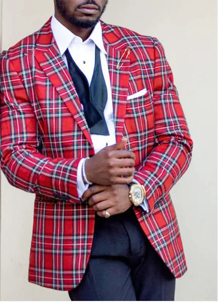 A stylish man wears a bold red plaid blazer with black, white, and yellow intersecting lines. Underneath, he sports a crisp white dress shirt with a loosely untied black bow tie, adding a relaxed yet sophisticated touch. A neatly folded white pocket square sits in the blazer’s breast pocket. He accessorizes with a gold wristwatch, a beaded bracelet, and a lapel pin. His black dress pants complement the ensemble, creating a striking and elegant look against the neutral background.