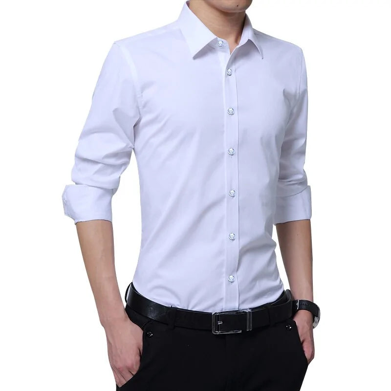 A stylish man wearing a fitted white dress shirt with long sleeves rolled up to the elbows. The shirt has a crisp collar and white buttons, giving it a sharp and professional look. He is also wearing black dress pants with a black belt featuring a silver buckle. His hands are casually placed in his pockets, and he has a black wristwatch on his left wrist, completing the modern and elegant outfit