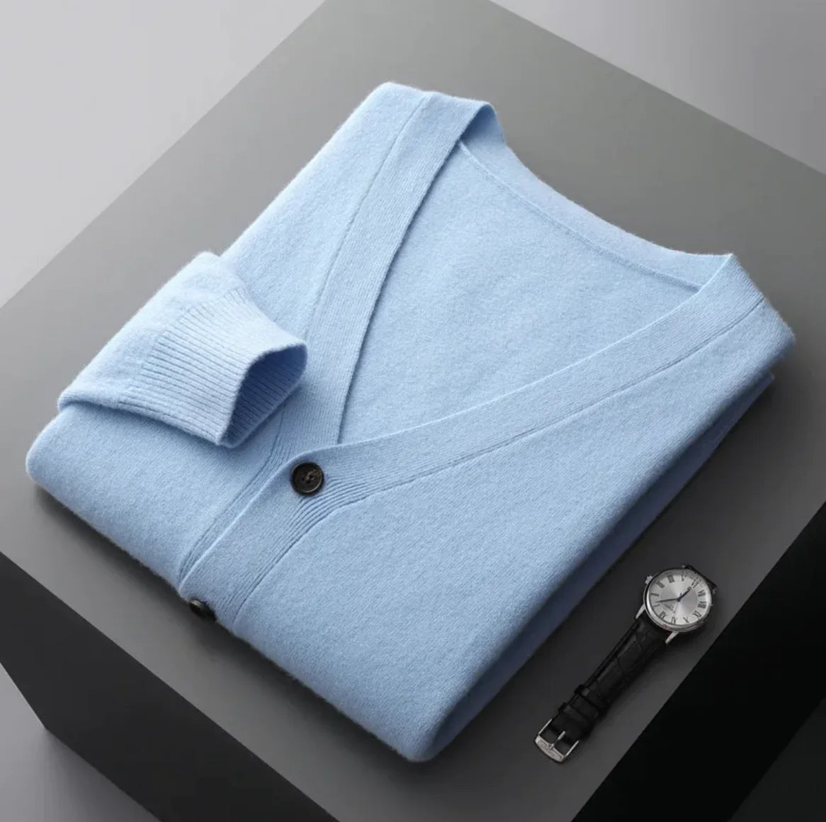 A neatly fold shirt on a black surface with a black wrist watch near it
