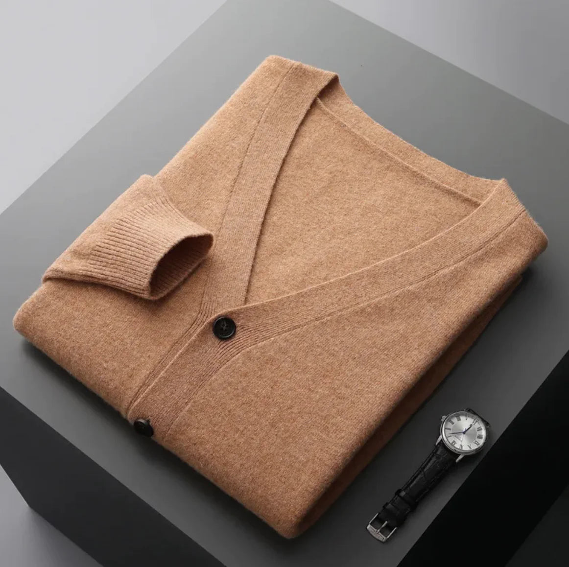 A neatly fold shirt on a black  surface with a black leather wrist-watch beside it
