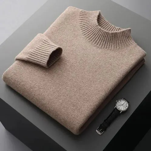 A neatly folded beige knitted sweater with a ribbed high collar and cuffs, placed on a dark grey surface. Beside the sweater, a classic wristwatch with a black leather strap and a silver dial is positioned, adding a touch of elegance to the composition.