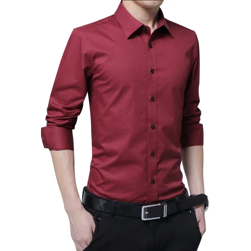 A stylish slim-fit burgundy dress shirt with long sleeves, buttoned cuffs, and a pointed collar. The shirt is paired with black dress pants and a black leather belt with a silver buckle. The model has the sleeves slightly rolled up, giving the outfit a smart-casual look.