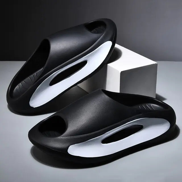 A pair of stylish black slip-on sandals with purple cushioned insoles, featuring cutout designs on the sides and toes, displayed on a white surface next to stacked books.