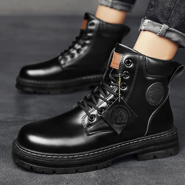 A pair of sleek black leather ankle boots with rugged rubber soles, lace-up fronts, and metal eyelets, displayed on a gray fabric surface with one boot propped up on a vintage-style book for presentation.