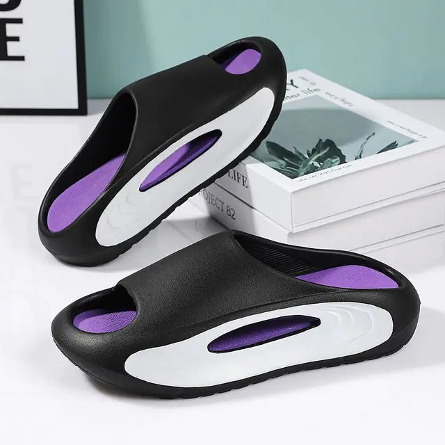 A pair of stylish black slip-on sandals with purple cushioned insoles, featuring cutout designs on the sides and toes, displayed on a white surface next to stacked books.