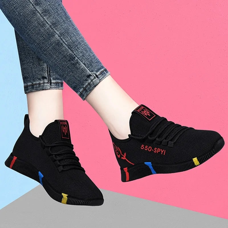 A pair of stylish black mesh sneakers worn with jeans. The shoes feature colorful embroidered details including a red and yellow daisy on the side and multicolored accents (red, blue, yellow) on the sole. The tongue displays a purple and red logo with the word "FASHION." The sneakers have a sleek, breathable design and a casual, trendy aesthetic.