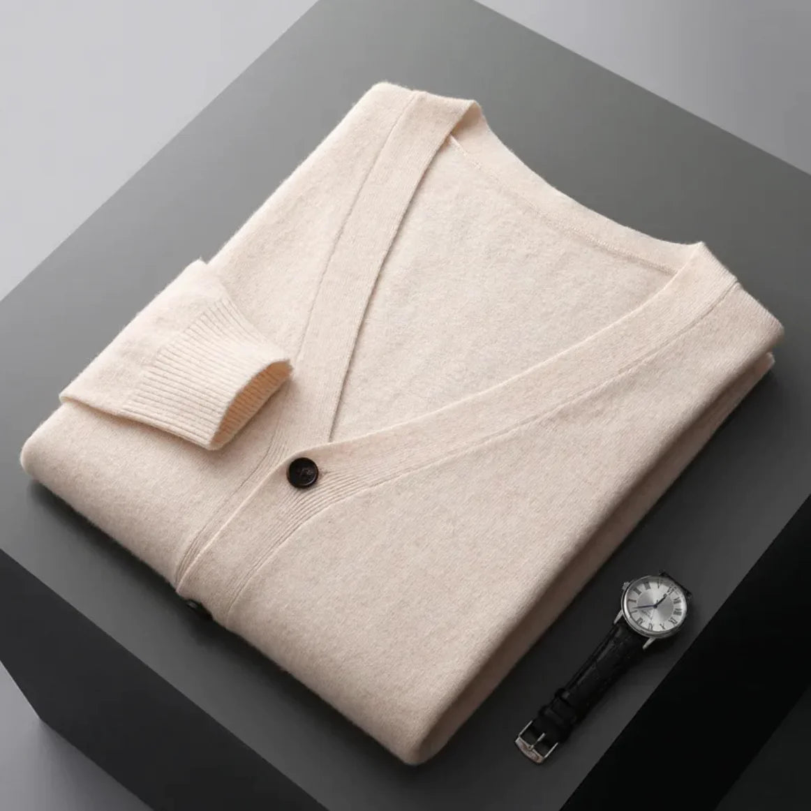 A neatly fold shirt on a black  surface with a black leather wrist-watch beside it