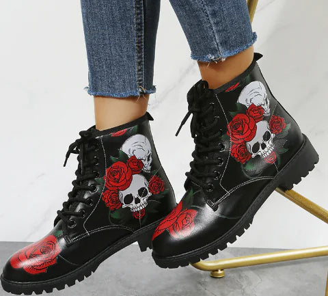 Black lace-up boots with skull and rose designs on a light gray background