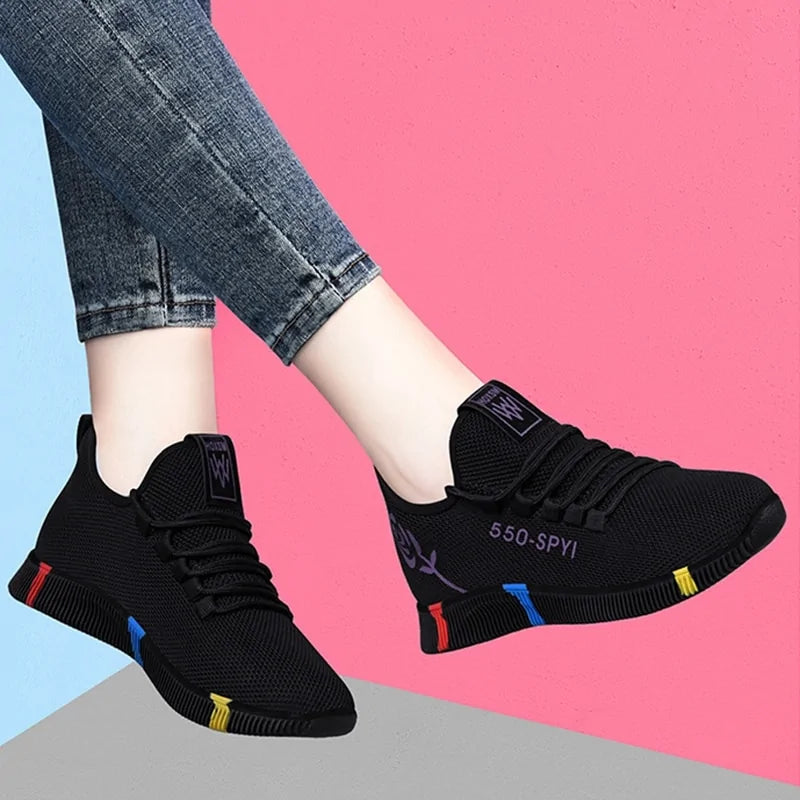 A pair of stylish black mesh sneakers worn with jeans. The shoes feature colorful embroidered details including a red and yellow daisy on the side and multicolored accents (red, blue, yellow) on the sole. The tongue displays a purple and red logo with the word "FASHION." The sneakers have a sleek, breathable design and a casual, trendy aesthetic.