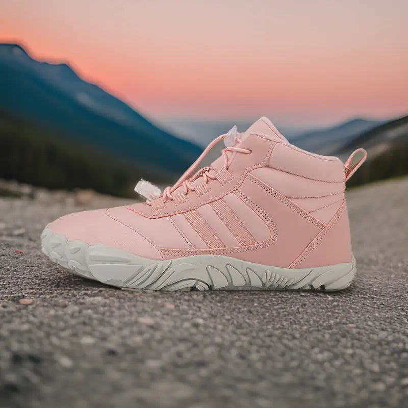 A single boot with black sole and subtle stripe detailing, placed on a rocky surface with a scenic backdrop of layered mountain ranges and a soft, pastel-colored sky at dusk or dawn.
