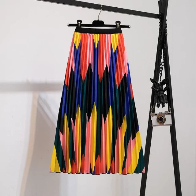 Pleated midi skirt with a gradient design, transitioning from dark black at the waistband to a soft blush pink at the hem, hanging on a black clothing rack next to a vintage-style camera.