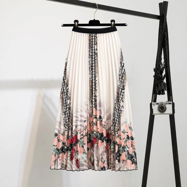 Pleated midi skirt with a gradient design, transitioning from dark black at the waistband to a soft blush pink at the hem, hanging on a black clothing rack next to a vintage-style camera.