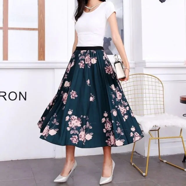 Pleated midi skirt with a gradient design, transitioning from dark black at the waistband to a soft blush pink at the hem, hanging on a black clothing rack next to a vintage-style camera.