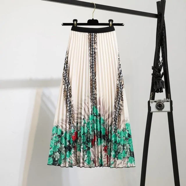 Pleated midi skirt with a gradient design, transitioning from dark black at the waistband to a soft blush pink at the hem, hanging on a black clothing rack next to a vintage-style camera.