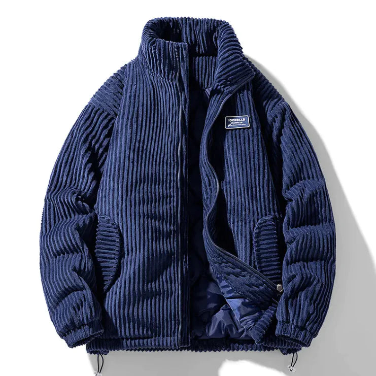 A stylish corduroy jacket with a plush fur-lined collar and inner lining is displayed against a white background. The jacket features a quilted black interior for added warmth, ribbed black cuffs and hem, and a zippered front closure. It has two side pockets, one of which has a small black and red tag. A subtle embroidered patch is visible on the left sleeve, adding a touch of detail to the design