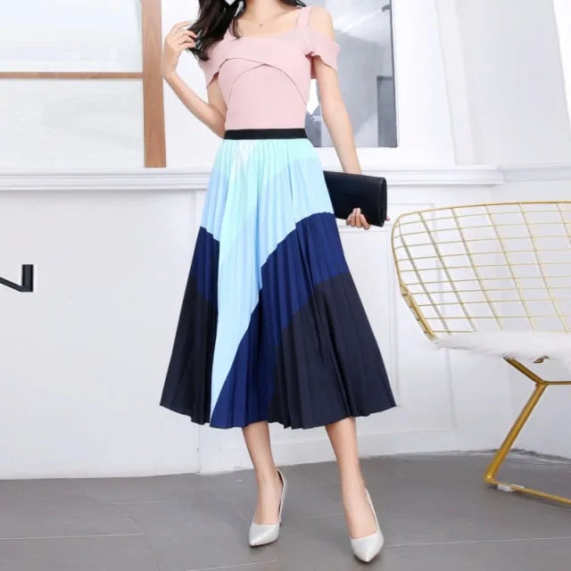 Pleated midi skirt with a gradient design, transitioning from dark black at the waistband to a soft blush pink at the hem, hanging on a black clothing rack next to a vintage-style camera.