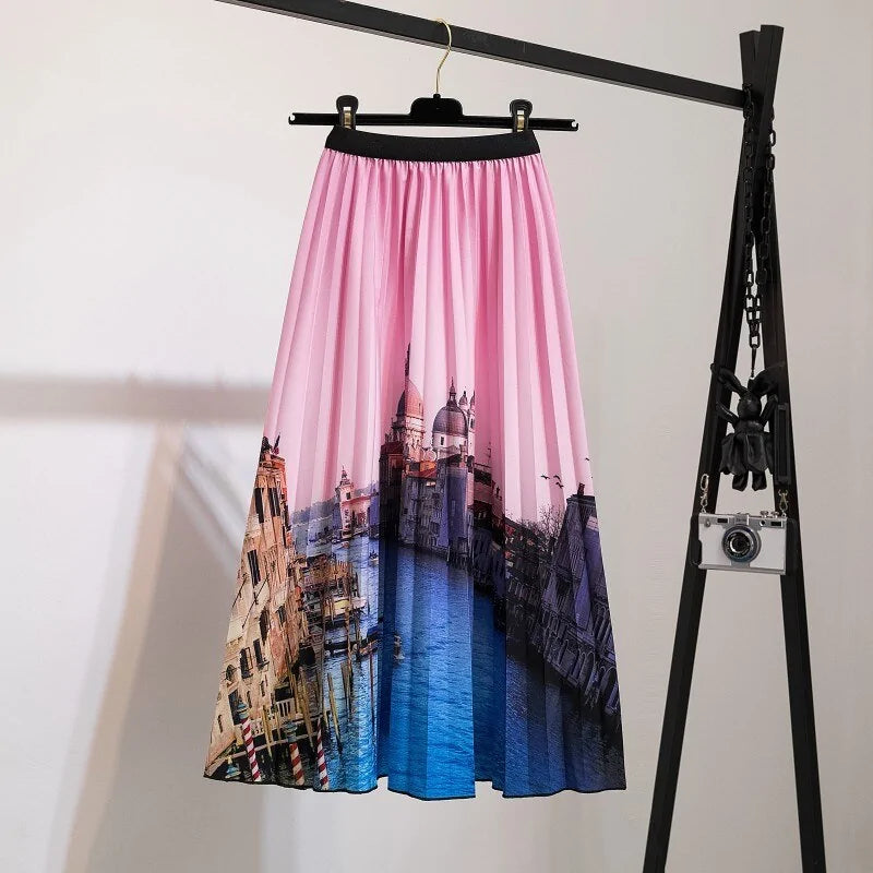 Pleated midi skirt with a gradient design, transitioning from dark black at the waistband to a soft blush pink at the hem, hanging on a black clothing rack next to a vintage-style camera.