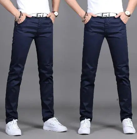 A pair of slim-fit burgundy pants is showcased by a model in two poses against a neutral gray background. The pants are paired with a white belt featuring a bold black buckle design, a white tucked-in shirt, and white sneakers. The model wears a wristwatch and bracelets, adding a stylish touch. The pants have a sleek, modern fit, emphasizing a trendy and casual yet polished look.