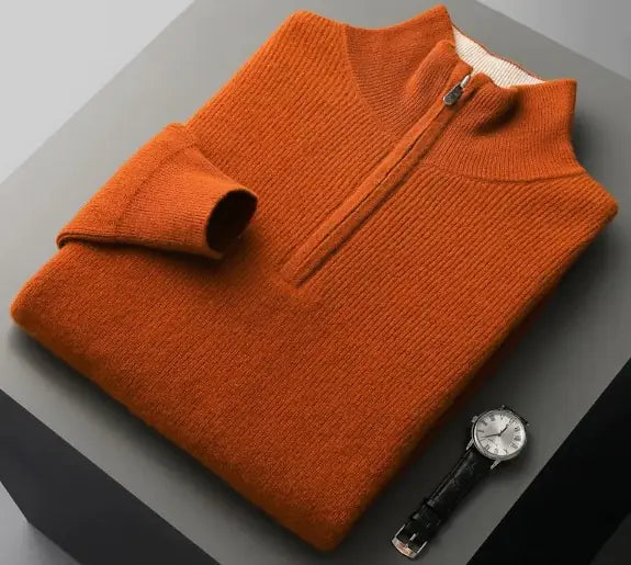 A neatly folded beige knitted sweater with a ribbed high collar and cuffs, placed on a dark grey surface. Beside the sweater, a classic wristwatch with a black leather strap and a silver dial is positioned, adding a touch of elegance to the composition.