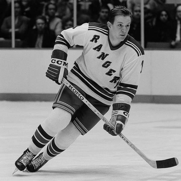 A black-and-white, square-format photo showing a vintage New York Rangers hockey player in full uniform mid-game. The player wears a classic jersey with bold detailing and holds a hockey stick while skating across the rink