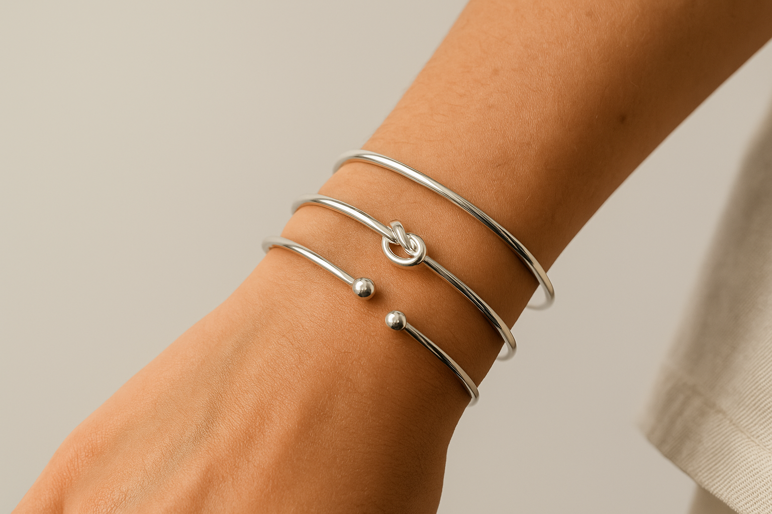 Close-up of a person’s wrist wearing three adjustable minimalist silver cuff bracelets against a soft neutral background.