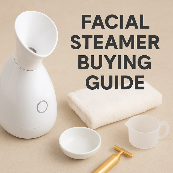 White tabletop facial steamer with a round button sits beside a folded cream towel, small white ceramic dish, clear plastic measuring cup, and a gold facial massage tool on a beige background.