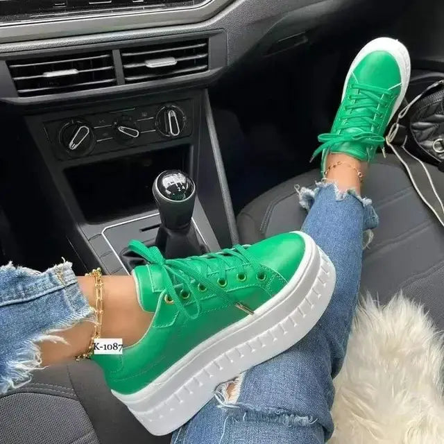 A pair of vibrant green platform sneakers worn by a person sitting in a car, with ripped blue jeans and a gold ankle bracelet. The sneakers feature white soles and are placed on the car’s floor.