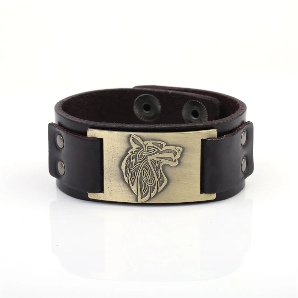 Black leather cuff bracelet with snap closure and a brass-toned rectangular plate engraved with a wolf head design, shown on a white background.